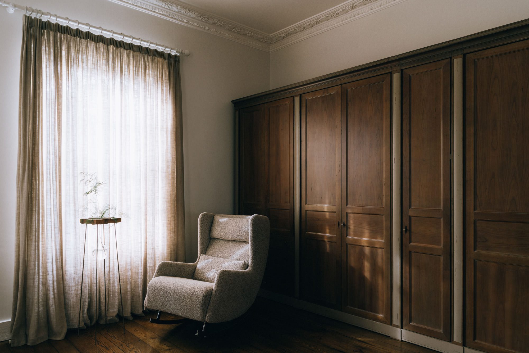 A detailed capture of the interior of a room, featuring a sofa, with brown wardrobes in the background and a curtain on the side, skillfully photographed by Brett Charles for interior architecture photography in the UK.